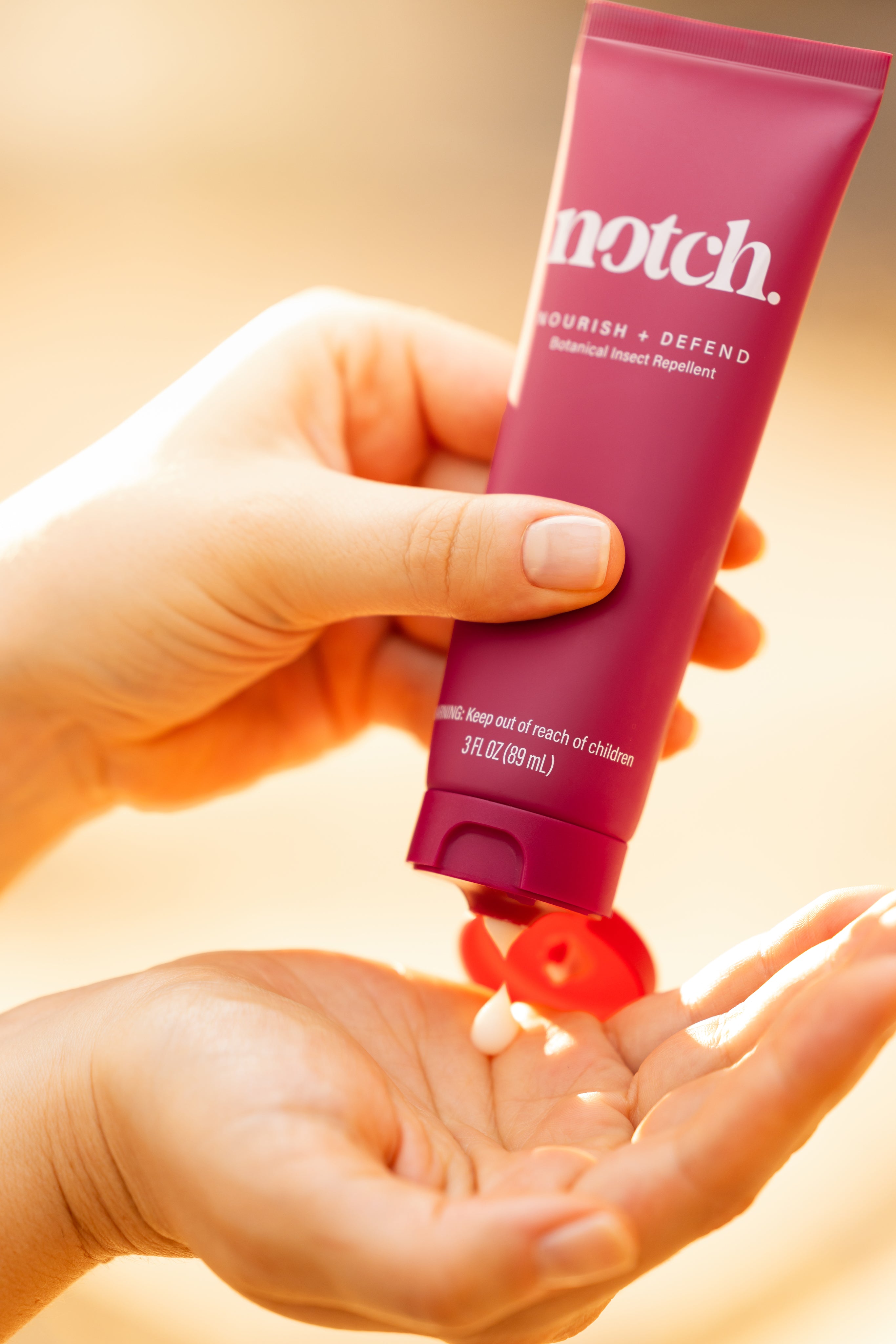 Hand holding a burgundy tube labeled 'notch' with a small amount of product on the palm against a warm beige background.